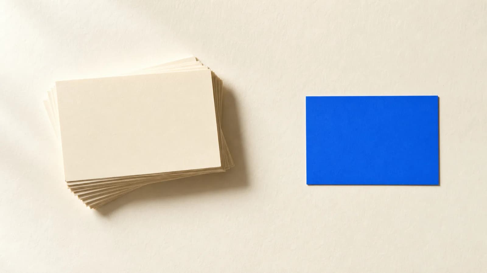 Identically sized paper cards stacked on a paper surface, with a single cobalt blue card standing apart at the edge