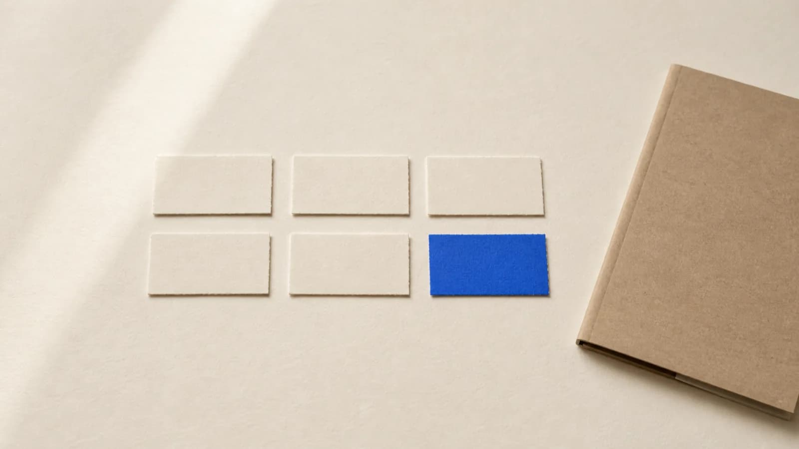 Six paper strips laid out neatly on a paper surface, one of them cobalt blue, with a thin folder at the edge