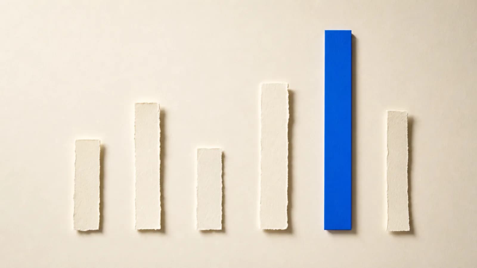 Paper strips of different lengths laid out on the floor; among the torn edged cream strips sits one long cobalt strip with cleanly cut edges.