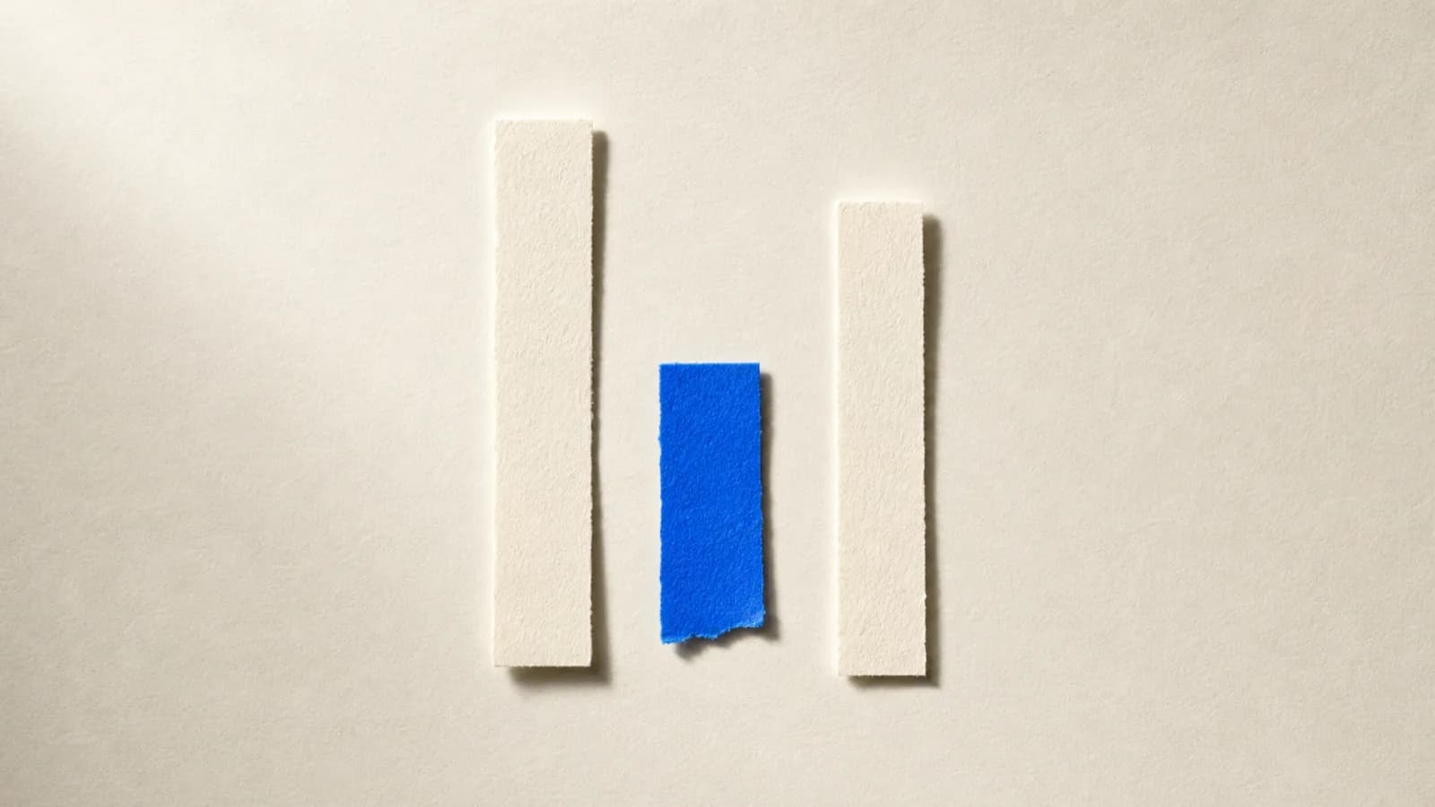 Three thin paper strips laid one under another on a paper surface; two cream, one cobalt blue and shorter than the rest
