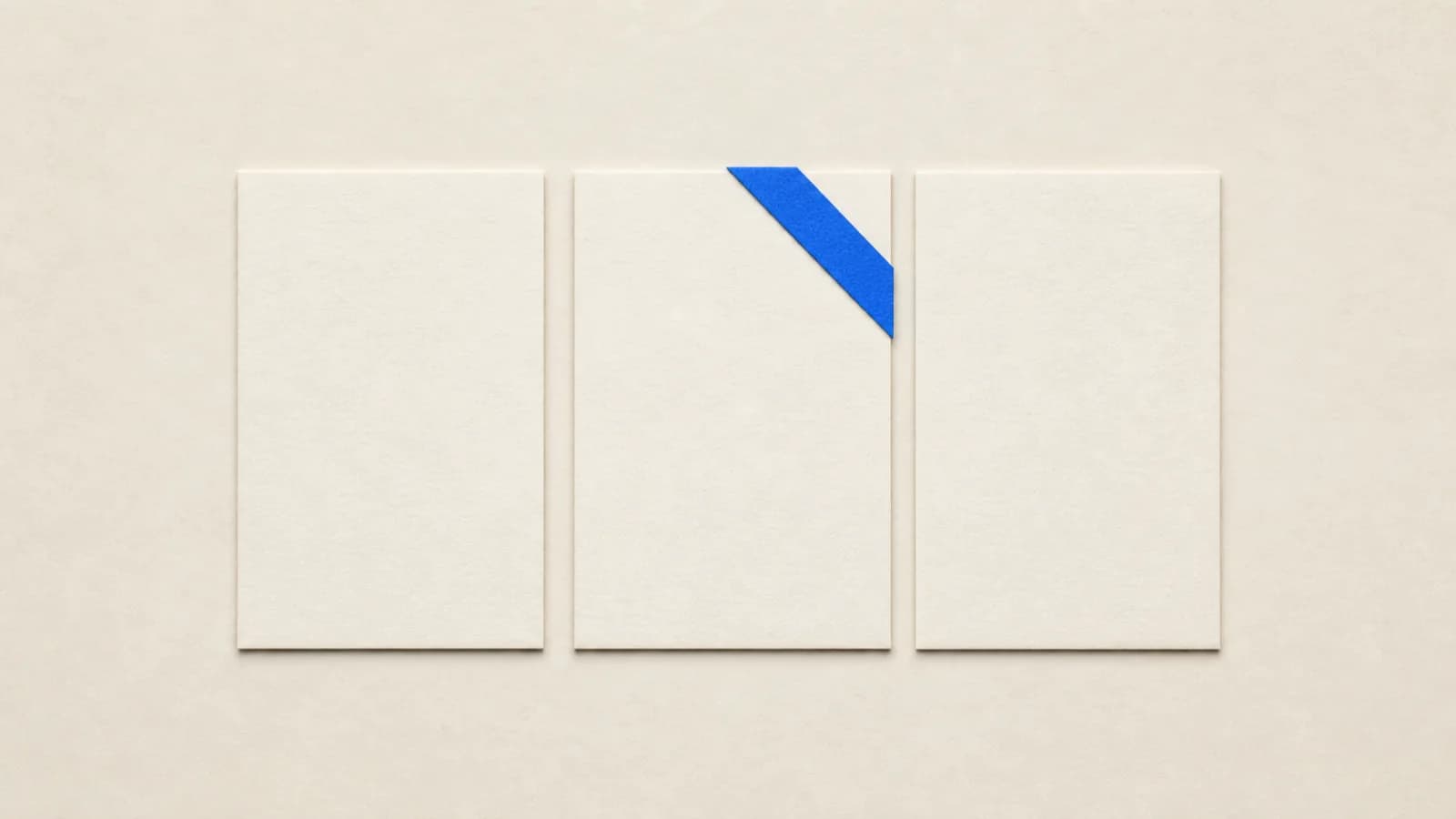 Three identical paper cards side by side on a paper surface; the middle one carries a cobalt blue strip on its corner