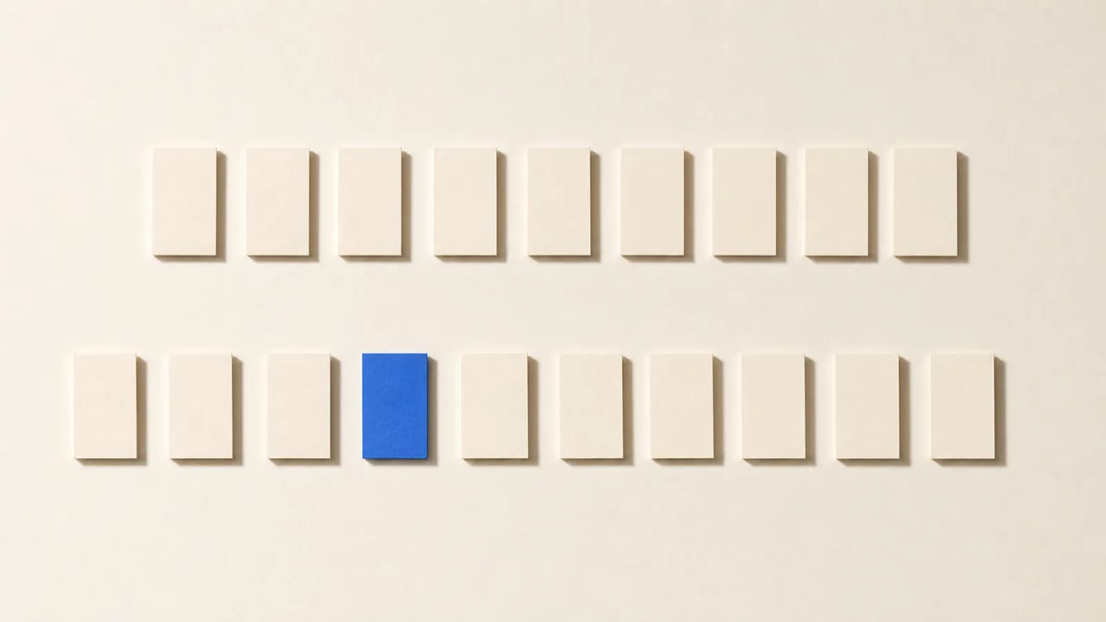 Paper cards laid out in two separate rows on an off white paper surface, one card in the lower row cobalt blue