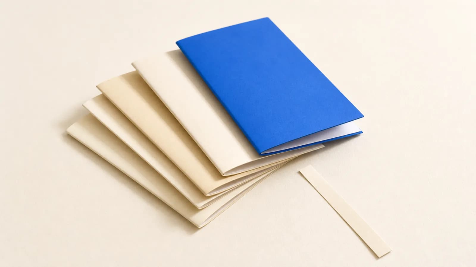 Five paper folders fanned out on an off white surface, the top one cobalt blue, an empty paper strip beside them