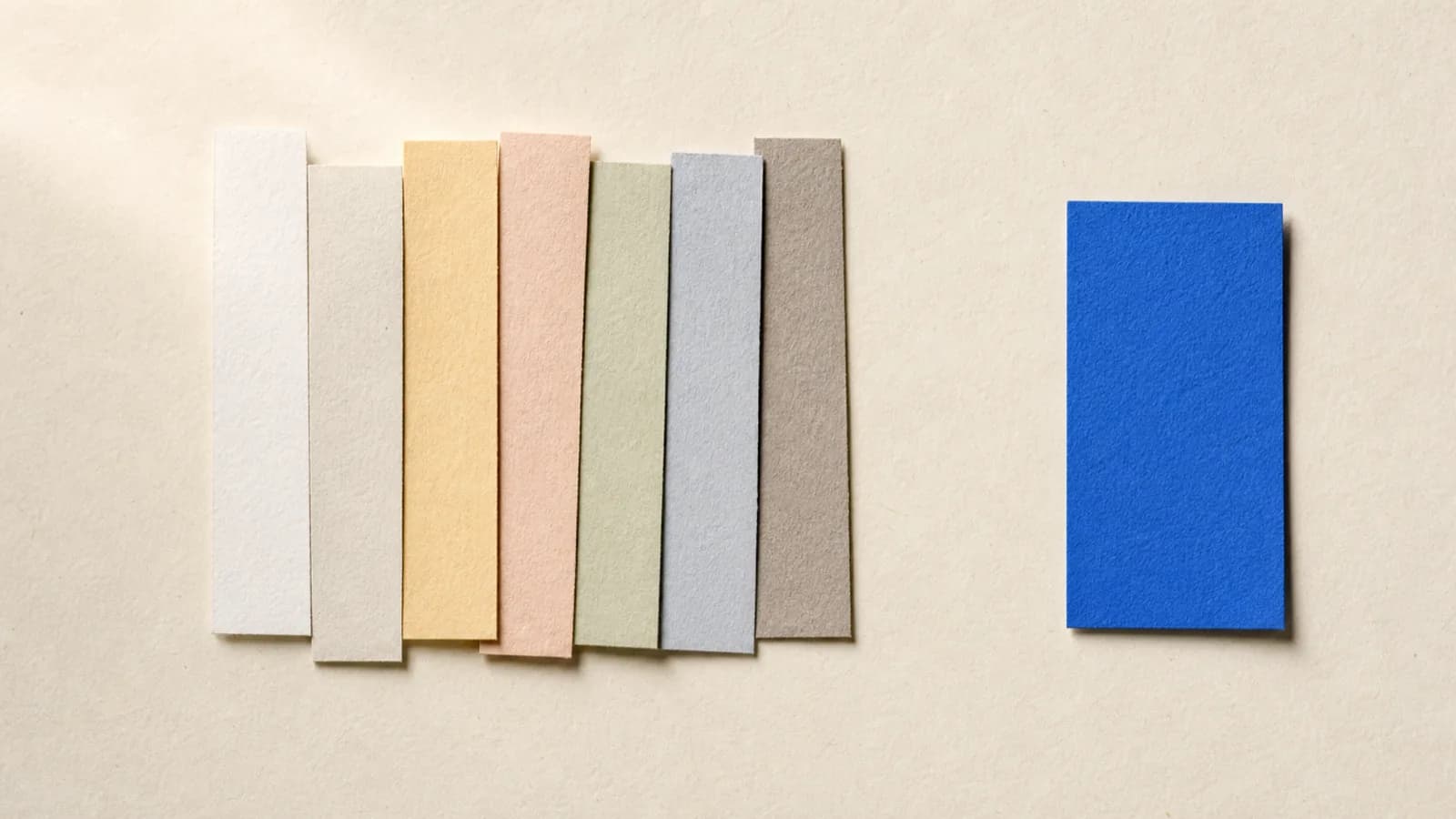 Seven paper strips gathered together on an off white surface, with a single cobalt blue card left on its own a few steps away