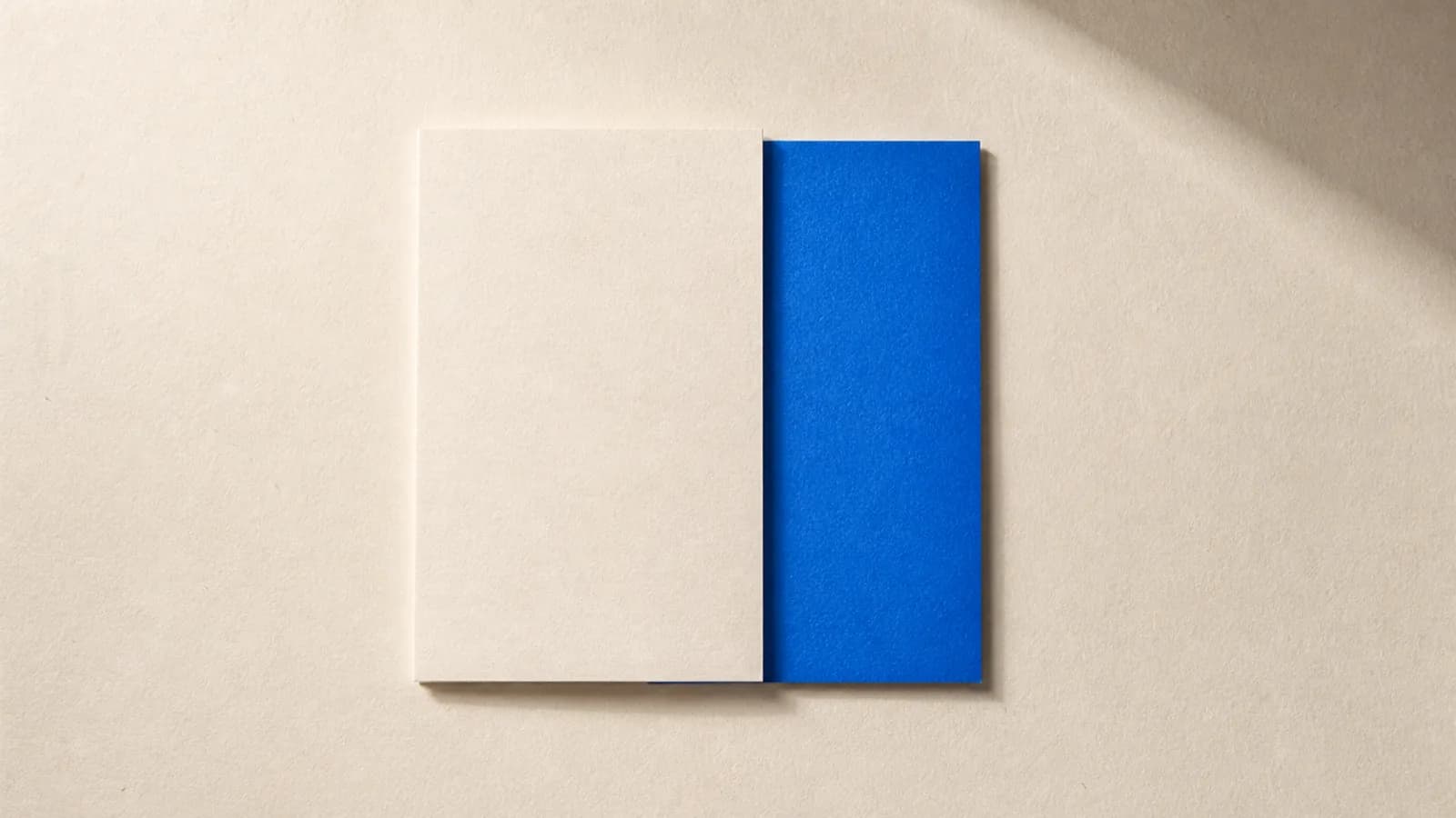 Two sheets of paper laid over each other on an off white surface, half of the blank cobalt blue card underneath hidden by the sheet on top